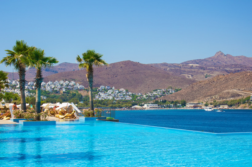 Infinity-Pool eines Luxushotels an der türkischen Ägäis mit Meerblick, Palmen, Sonnenliegen und weißer Küstenarchitektur