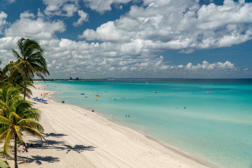 Traumhafter Strand von Varadero auf Kuba mit weißen Sandstränden, Palmen, türkisblauem Meer und badenden Urlaubern unter leicht bewölktem Himmel – eines der beliebtesten Reiseziele der Karibik.