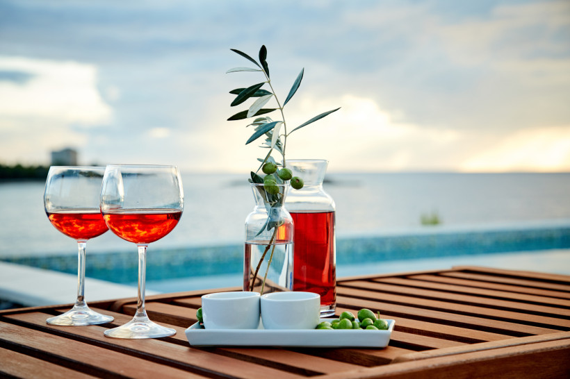 Mallorca Zwei Gläser Roséwein, Oliven und eine Karaffe auf einem Holztisch mit Meerblick bei Sonnenuntergang