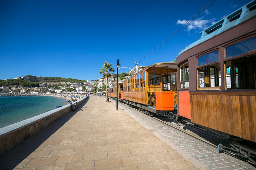 Straßenbahn am Hafenboulevard von Port de Sóller mit Strand und Bucht im Hintergrund