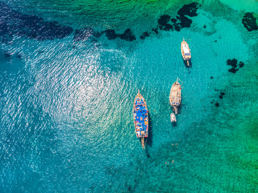 Luftaufnahme von mehreren Ausflugsbooten im kristallklaren, türkisfarbenen Meer vor der Küste von Bodrum