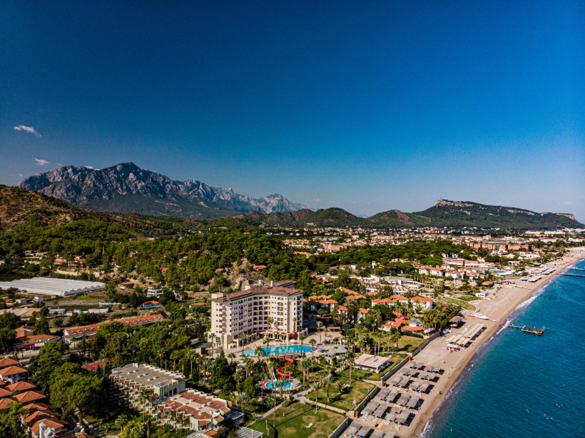 Luftaufnahme von Çamyuva bei Kemer mit Strandhotels, Kiesstrand, türkisblauem Meer und dem Taurusgebirge im Hintergrund