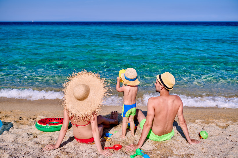 Familie am Sandstrand an der Küste, sitzend und spielend am Wasser