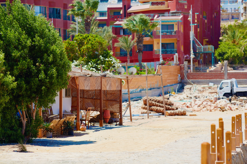Weiße Sandinsel mit türkisfarbenem Wasser, Strohhütten und Booten vor einer kargen Inselkulisse.