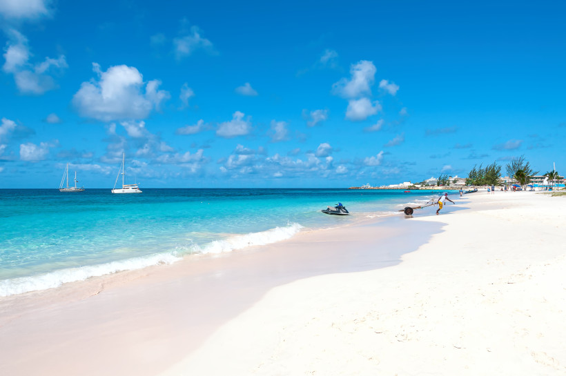 Traumstrand in der Karibik – Barbados mit türkisblauem Wasser und weißen Segelbooten Weißer Sandstrand auf Barbados mit türkisblauem Meer, Jet-Ski und Segelbooten bei blauem Himmel.