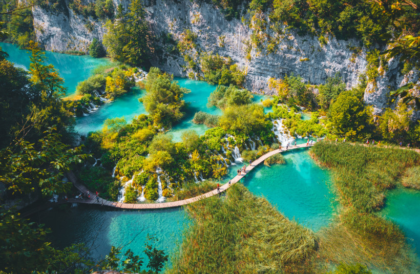 Wasserfälle des Nationalparks Plitvicer Seen, Kroatien Holzsteg führt durch türkisfarbene Seenlandschaft mit Wasserfällen, üppiger Vegetation und steilen Felswänden im Plitvicer Nationalpark in Kroatien