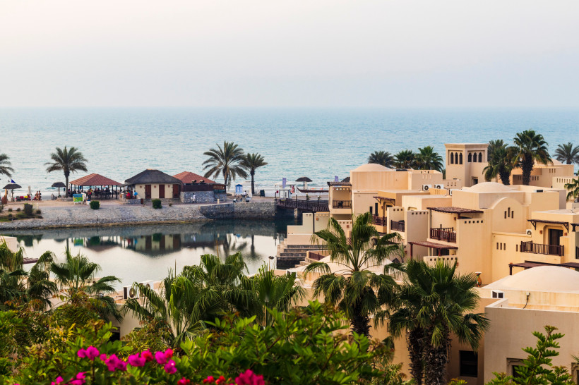 Ras al Khaimah, budgetfreundlicher Urlaub Resort mit traditionellen Sandsteinbauten, Palmen und Blick auf das Meer bei Sonnenuntergang