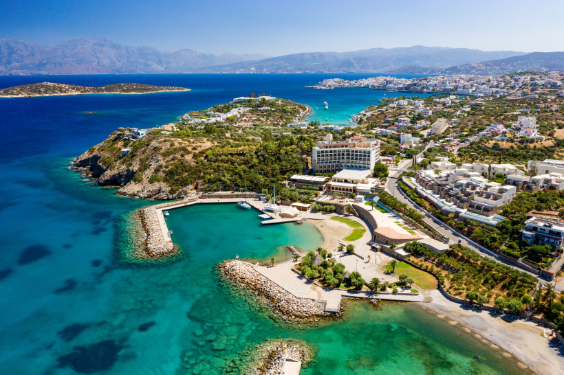Panoramablick über die Mirabello-Bucht bei Agios Nikolaos mit türkisfarbenem Meer, Küste, Hafenbecken und Bebauung am Hang