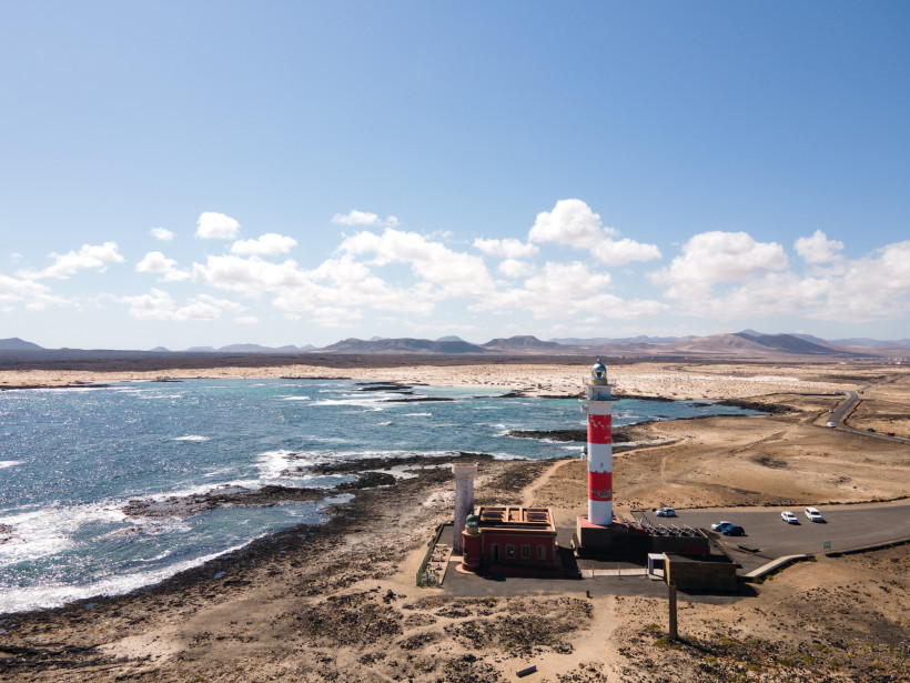 Faro del Tostón, rot-weiß gestreifter Leuchtturm an der felsigen Küste mit Meer und karger Landschaft
