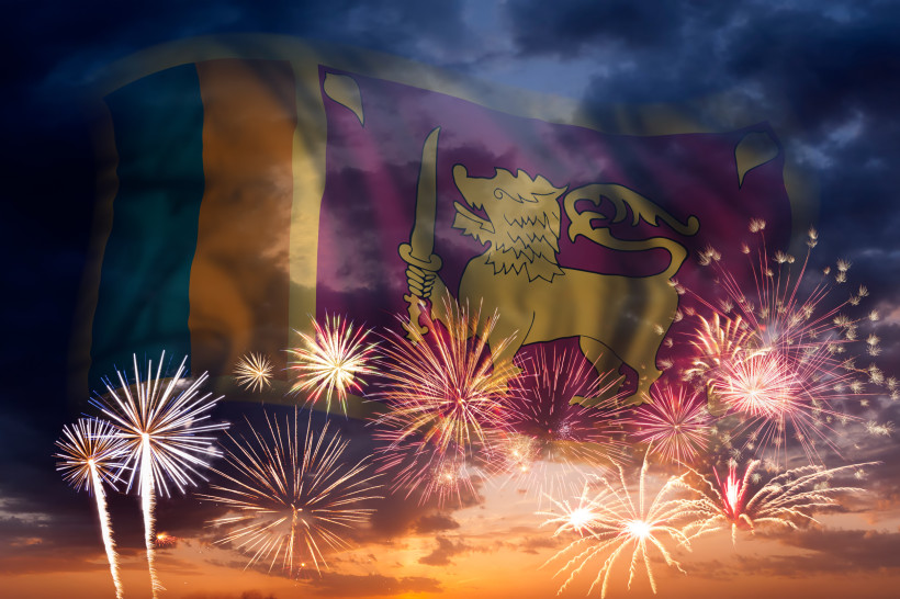 Die Flagge Sri Lankas mit dem goldenen Löwen ist transparent über ein farbenfrohes Feuerwerk am Abendhimmel gelegt.