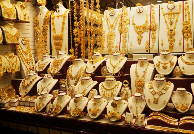 Auslage in einem Schaufenster des Gold Souk in Dubai. Zu sehen sind zahlreiche goldene Schmuckstücke wie Ketten, Ringe, Armbänder und Ohrringe, kunstvoll arrangiert auf weißen Büsten. Die Goldstücke funkeln im warmen Licht und zeigen orientalische Designs