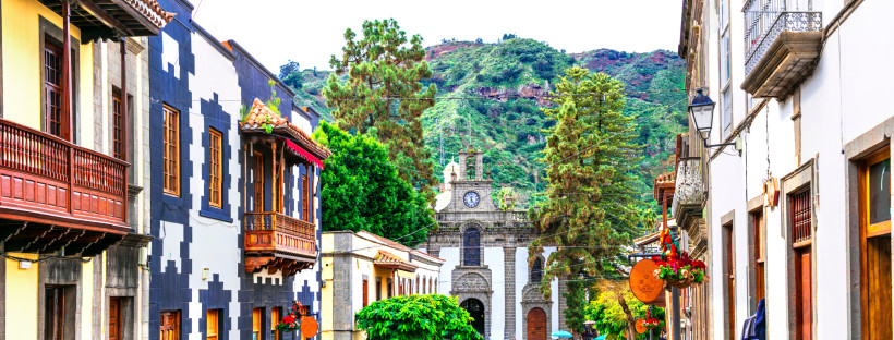 Blick auf die Altstadt von Teror auf Gran Canaria mit bunten traditionellen Häuserfassaden und Holzbalkonen, im Hintergrund die Basilika Nuestra Señora del Pino vor grünen Bergen.
