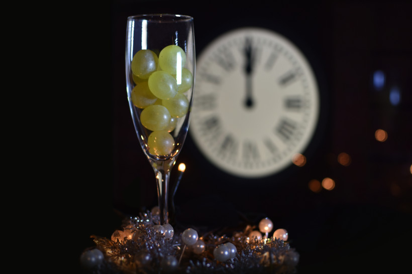 Fuerteventura Ein Sektglas gefüllt mit zwölf grünen Trauben, im Hintergrund eine Uhr, die Mitternacht anzeigt – symbolisch für den spanischen Silvesterbrauch.