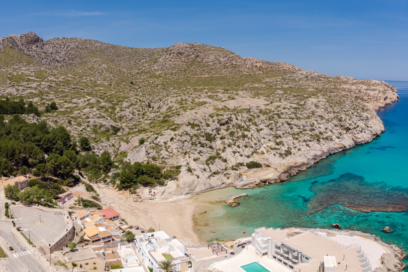 Luftaufnahme der Cala Barques in Cala San Vicente mit Sandstrand, türkisfarbenem Wasser und umliegender Felslandschaft der Nordküste Mallorcas.