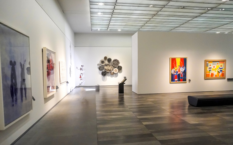 Innenansicht einer modernen Kunstgalerie mit abstrakten Gemälden, Skulpturen und Installationen an weißen Wänden unter einem verglasten Dach