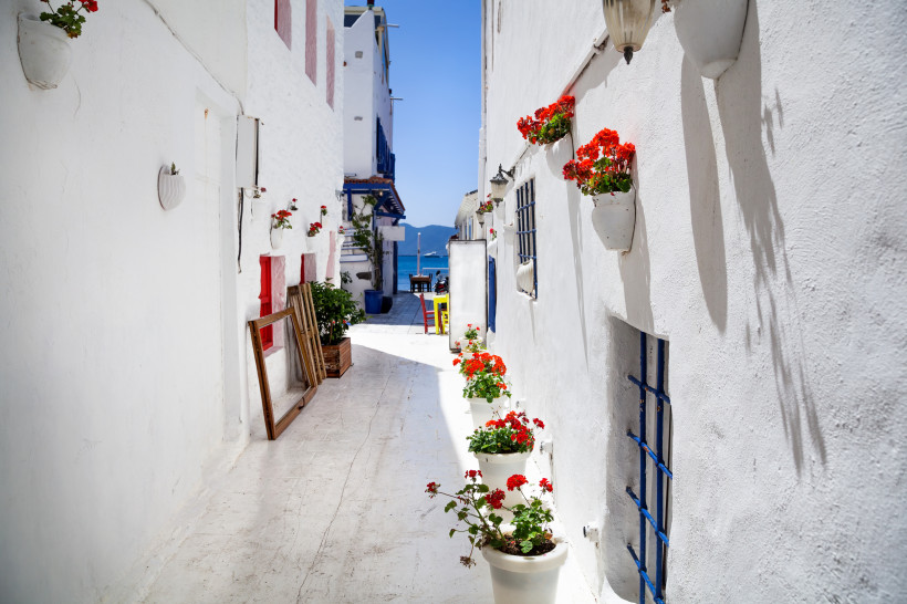 Schmale weiße Gasse mit roten Blumen und Blick auf das Meer in einem mediterranen Dorf