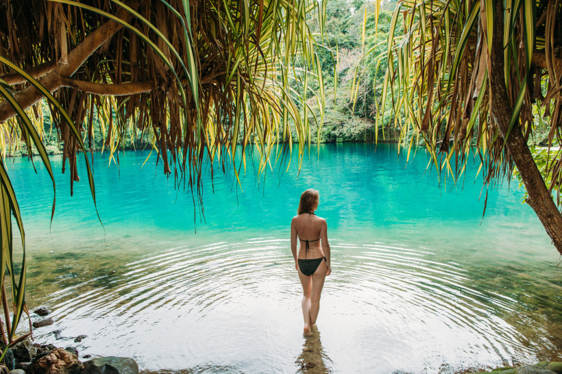 Türkisfarbene Lagune im Tropenparadies – idyllischer Naturpool zum Entspannen Frau im Bikini steht am Ufer einer türkisfarbenen Lagune, umgeben von tropischer Vegetation – idyllischer Naturpool inmitten des Dschungels.