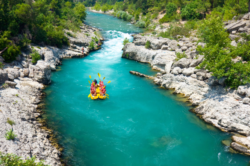 Gruppe von Menschen beim Rafting auf einem türkisblauen Fluss, umgeben von Felsen und grünem Wald in der Türkei