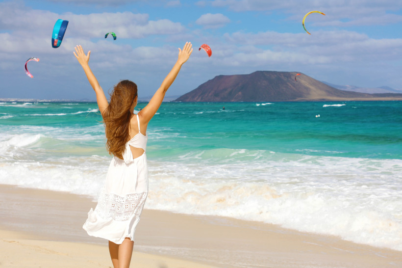 Frau am Strand von Corralejo mit Kitesurfern über türkisfarbenem Wasser
