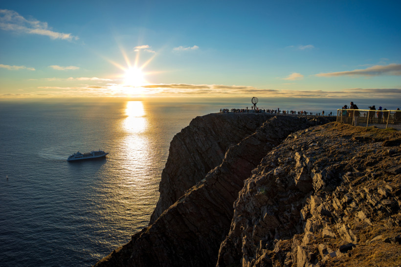Nordkap: Klippe mit Aussichtspunkt und Globus-Skulptur bei tief stehender Sonne über dem Meer Felsklippe am Nordkap mit Aussichtspunkt und Globus-Skulptur, tief stehende Sonne über dem Meer und Schiff im Wasser