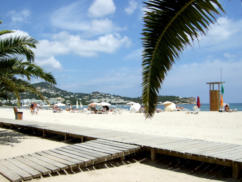 Strand Talamanca mit Holzsteg im Sand, Sonnenschirmen und Blick auf die Bucht