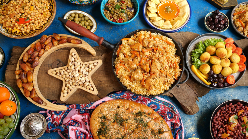 Ägypten Bunt gedeckter Tisch mit traditionellen orientalischen Speisen: Reispfanne mit Hähnchen, Falafel, Oliven, Datteln, Fladenbrot, Kichererbsensalat, süße Gebäckstücke und Nüsse in einem Holztablett in Form von Halbmond und Stern