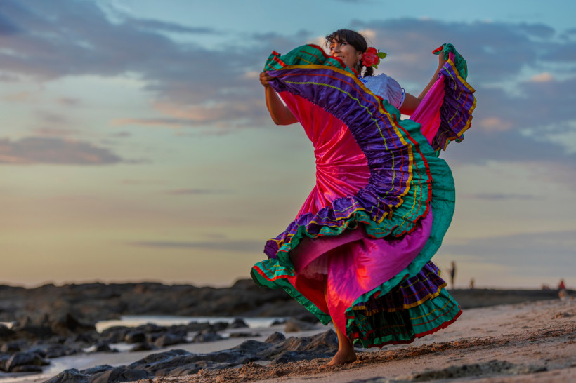Fiestas de Palmares, Costa Rica Frau in einem traditionellen, farbenfrohen Kleid tanzt folkloristisch am Strand bei Sonnenuntergang