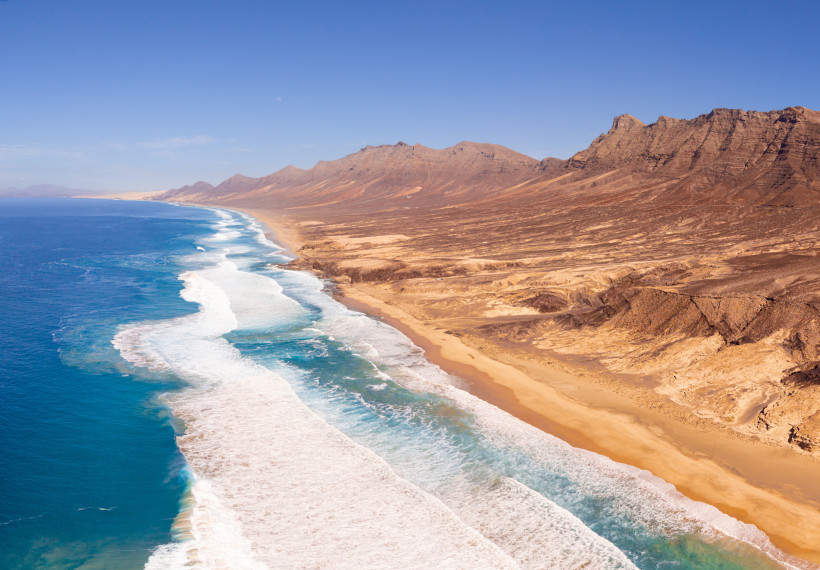Küstenlinie bei Jandía mit langem Sandstrand, Brandung und karger Berglandschaft