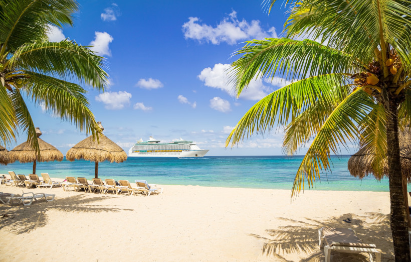 Kreuzfahrtschiff vor einer Karibikinsel, Blick vom Strand mit Palmen und Liegen