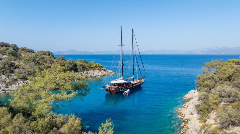 Segelboot vor der Küste von Kemer in einer ruhigen Bucht mit kristallklarem, türkisblauem Wasser und felsiger Landschaft