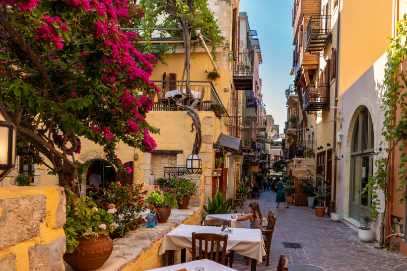 Altstadtgasse in Chania mit Bougainvillea und Cafétischen Gasse in der Altstadt von Chania mit Restaurants, Balkonen und blühender Bougainvillea