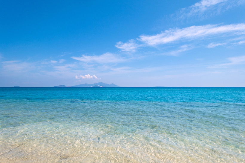 Kos Klares türkisfarbenes Meer mit flachem Wasser am Strand und Blick auf entfernte Inseln unter blauem Himmel mit leichten Wolken