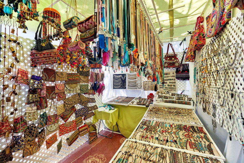 Ibiza - Hippiemarkt Punta Arabí Hippiemarkt auf Ibiza: Ein Stand voller bunter Accessoires. An den Wänden hängen verzierte Handtaschen und Beutel mit Stickereien, während Tische mit Schmuck wie Ketten, Armbändern und Ringen bedeckt sind. Über dem Stand hängen viele Halsketten und dekora