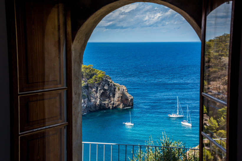 Mallorca Atemberaubender Blick aus einem offenen Fenster auf das blaue Meer, Klippen und Segelboote bei schönem Wetter auf Mallorca