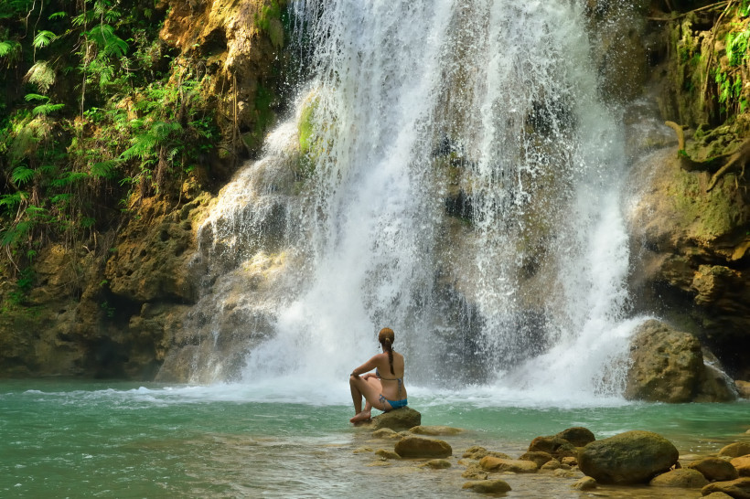 Dominikanische Republik Frau sitzt am Ufer und blickt auf den imposanten Wasserfall El Limón auf Samaná in der Dominikanischen Republik