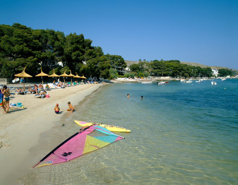 Sandstrand in Port de Pollença mit Badegästen, Sonnenschirmen und flachem, klarem Wasser