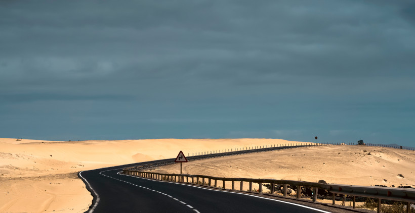 Kurvenreiche Straße durch die Sanddünen bei Corralejo unter bewölktem Himmel