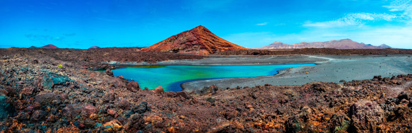 El Golfo – Die grüne Lagune von Lanzarote im Vulkankrater Grüne Lagune Charco de los Clicos vor rotem Vulkankegel im Nationalpark Timanfaya auf Lanzarote, umgeben von schwarzem Lavagestein