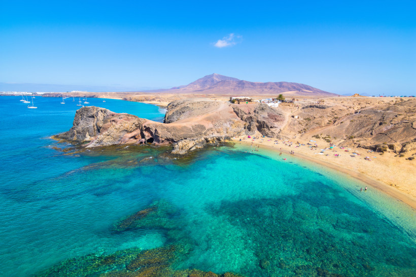 Bucht am Papagayo Beach auf Lanzarote mit türkisfarbenem Wasser, Felsen, Sandstrand und Booten vor der Küste