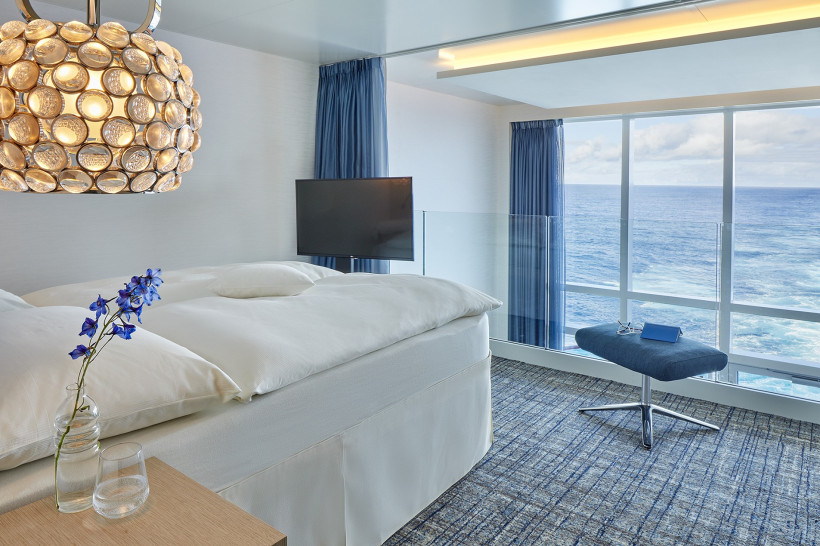 Schlafbereich einer Penthouse-Suite auf der AIDAnova mit großem Bett und Meerblick durch Panoramafenster