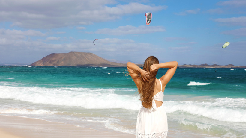 Strand in Corralejo mit Blick auf das Meer, eine Person im Vordergrund und Kitesurf-Schirme am Himmel