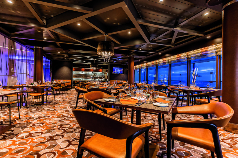 Gastraum des Steakhouse Surf und Turf auf Mein Schiff 6 mit gedeckten Tischen und großen Panoramafenstern