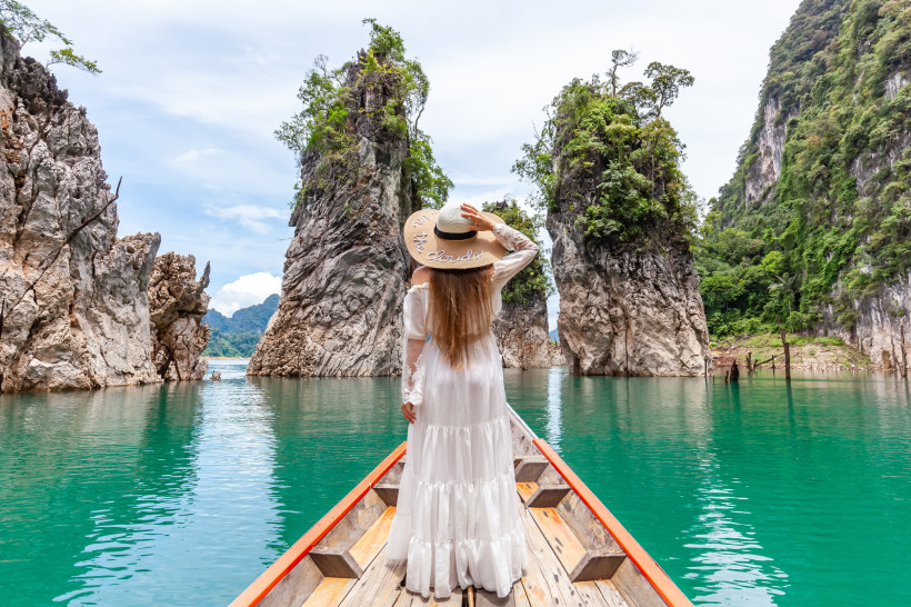 Thailand Süden – Longtailboot im Khao Sok Nationalpark vor Kalksteinfelsen Frau auf einem Longtailboot im Khao Sok Nationalpark in Südthailand, umgeben von türkisblauem Wasser und beeindruckenden Kalksteinfelsen.