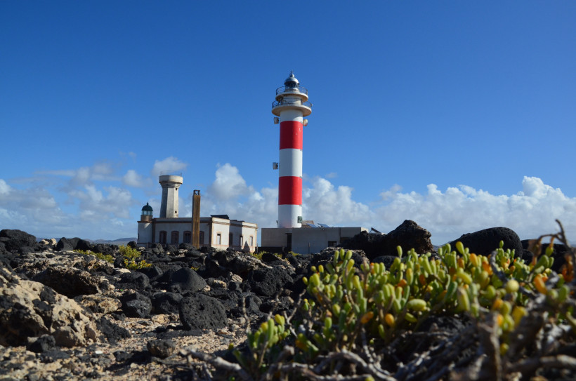 Leuchtturm Faro del Tostón mit rot-weißem Turm auf felsiger Küste unter blauem Himmel
