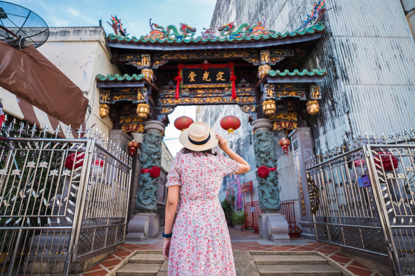 Frau in Sommerkleid steht vor traditionellem chinesischen Tor in Phuket Town, Thailand