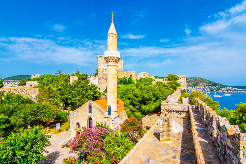 Historische Festungsanlage mit Minarett, Natursteinmauern und Blick auf das Meer