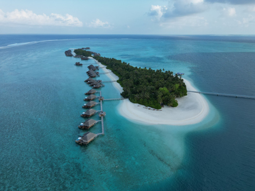 Luftaufnahme einer Insel auf den Malediven mit Palmen, Sandstrand und Wasserbungalows in türkisfarbenem Meer