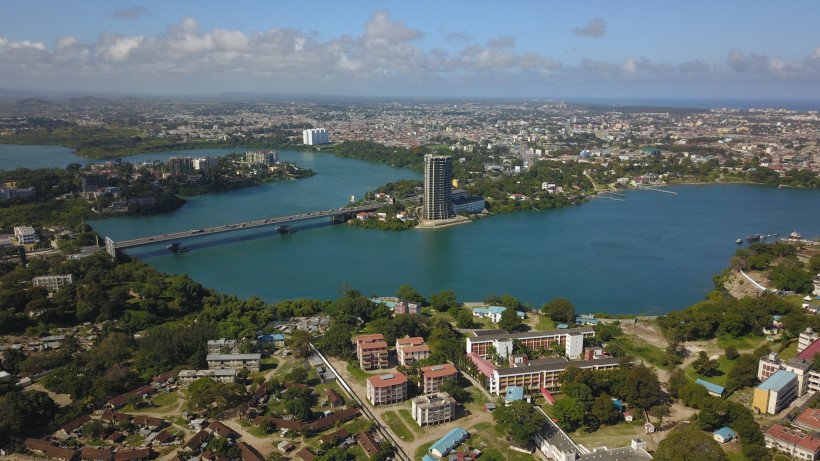 Kenia Luftaufnahme von Mombasa, einer Küstenstadt in Kenia. Zu sehen ist eine große Brücke über einem breiten Flussarm, umgeben von Hochhäusern, Wohngebieten und viel Grün. Am Horizont erstreckt sich die Stadt bis zum Meer