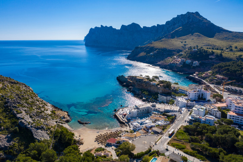 rohnenaufnahme von Cala San Vicente mit Badebucht, Hotels und steilen Felsformationen an der Nordküste Mallorcas.