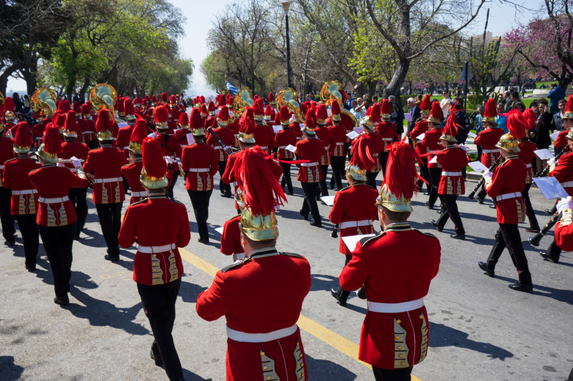Musik und Tradition auf Korfu: Die Stadtkapelle in markanten roten Uniformen mit goldenen Helmen zieht bei einem festlichen Umzug durch die Straßen. Die Kapelle spielt eine zentrale Rolle bei Feierlichkeiten und verleiht Festen wie Nationalfeiertagen eine
